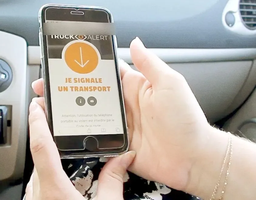 Une main tient un téléphone qui affiche TruckAlert et son bouton pour signaler un transport